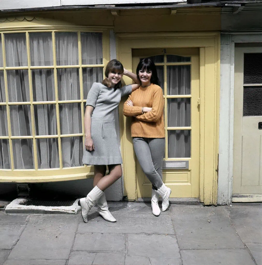 Olivia NewtonJohn left and Pat Carroll right standing outside home with yellow door
