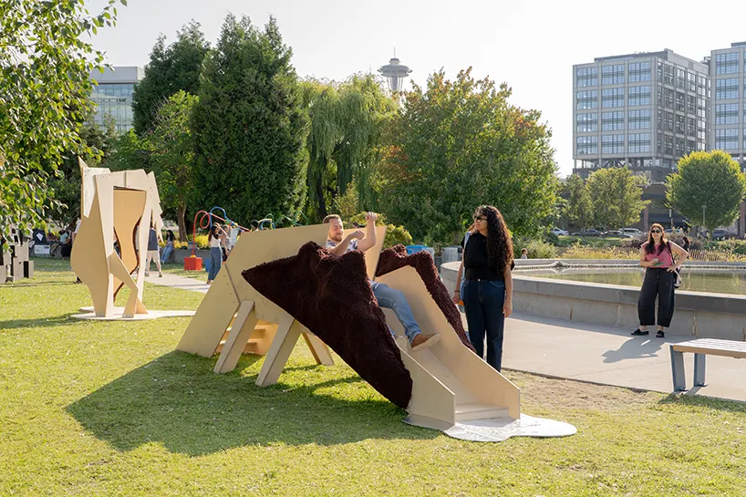 people of all ages sliding down Slide Horse, with the Space Needle in the background, immersed in a horse playground