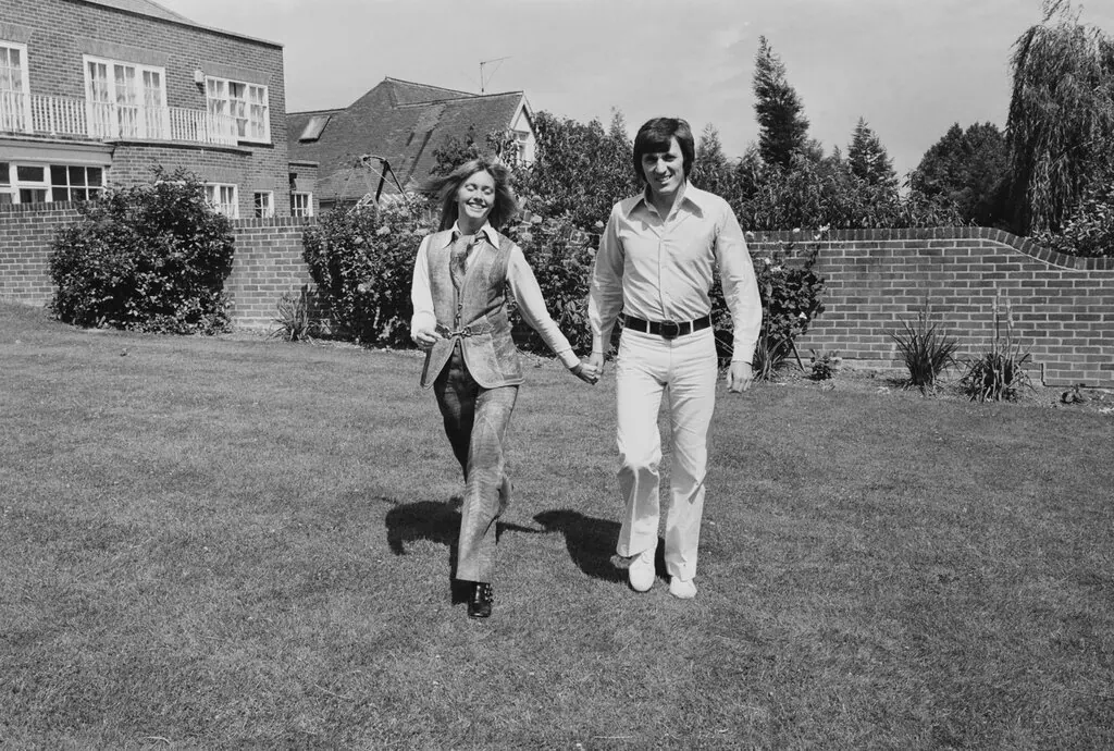 blackandwhite photo of Olivia NewtonJohn and Bruce Welch walking lawn of the Hadley Common home
