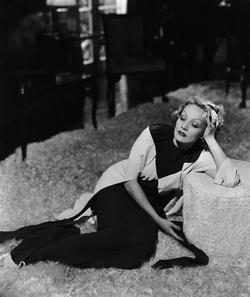 blackandwhite photo of Marlene Dietrich lounging on shag rug at home leaning against ottoman