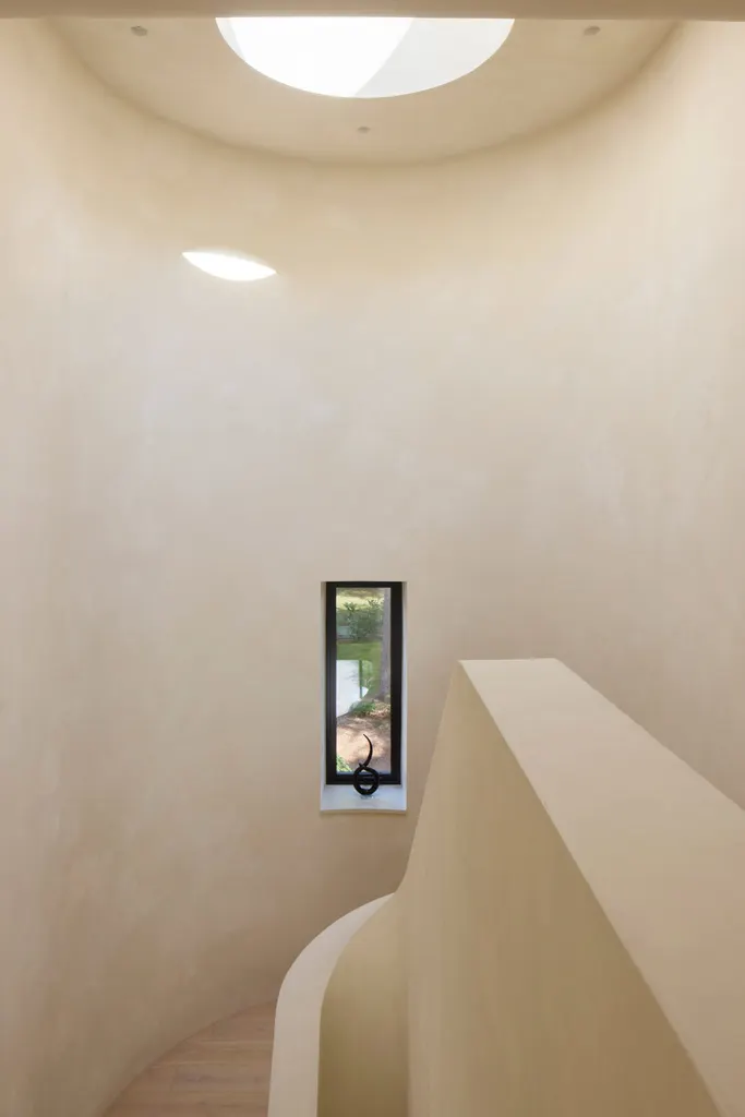 A curving staircase is illuminated by a circular skylight